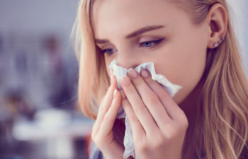 A sick woman using a tissue for runny nose.