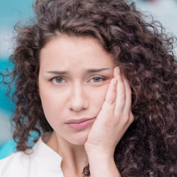 a woman with curly hair holds her cheek in pain