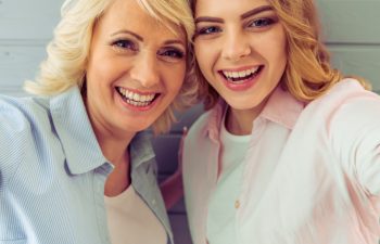 Broadly smiling young woman with her mother taking selfie.