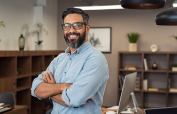 Portrait of happy mature businessman wearing spectacles and looking at camera. Multiethnic satisfied man feeling confident in a creative office. Successful middle eastern business man smiling.